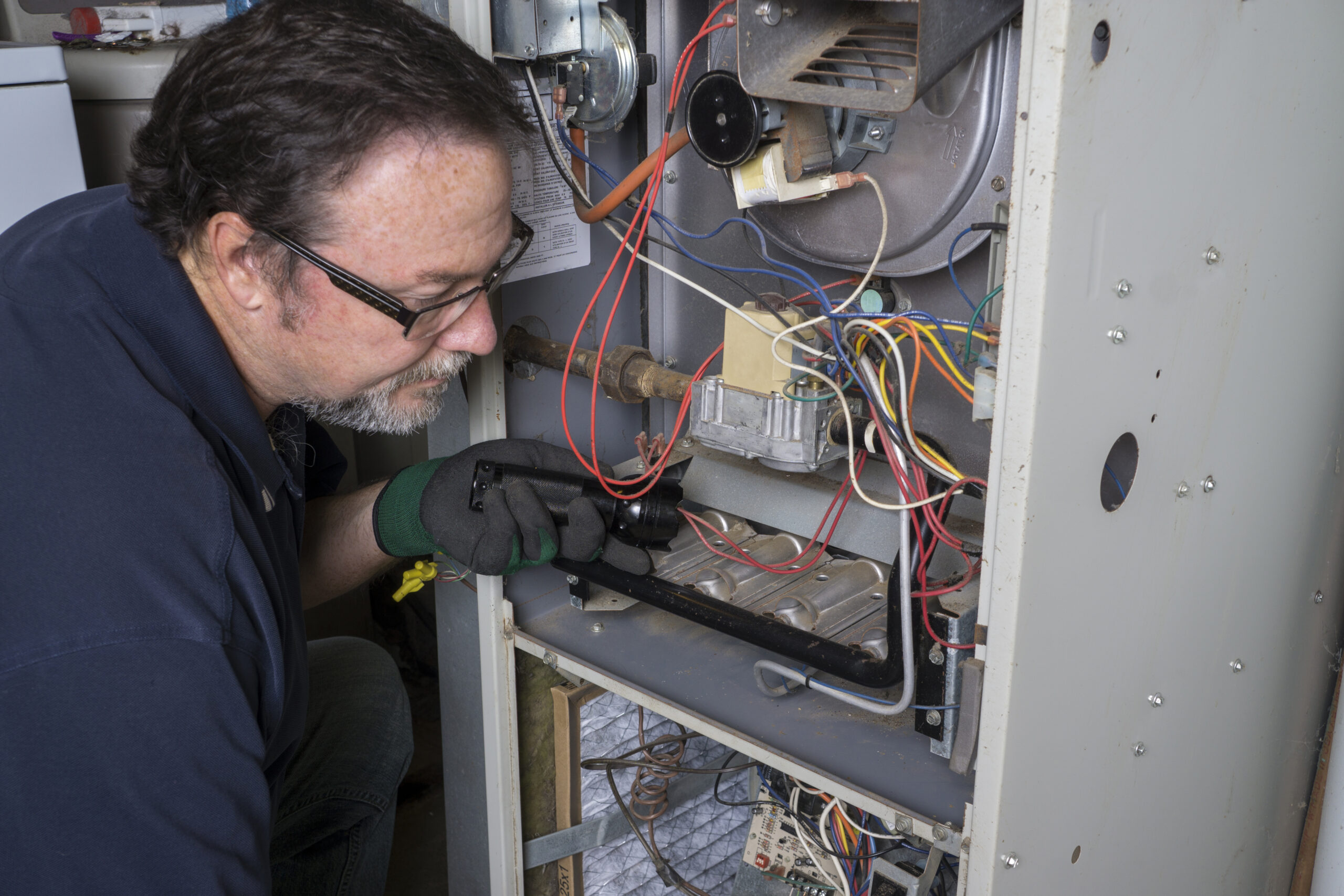 Technician inspecting an old furnace in a San Jose home before replacement